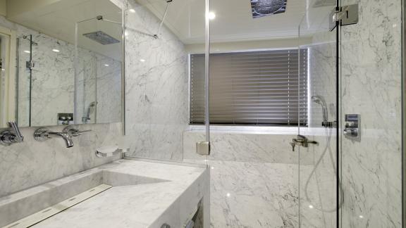 A bright marble bathroom with rain shower, chic fittings, large mirror and washbasin.